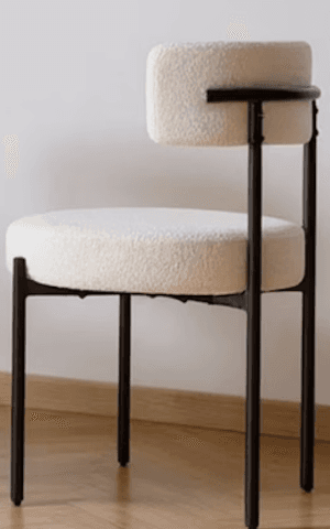 A modern accent chair with a black metal frame and a plush, textured cream-colored upholstery. The seat is round and thickly padded, and the backrest is a gently curved, low profile with a cylindrical armrest integrated into one side. The legs are slim and angled. — 3D model