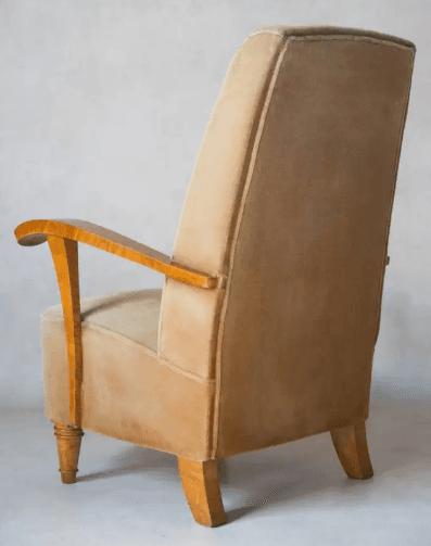 A vintage armchair with a high back and upholstered in a light brown, velvety fabric. The armrests are made of polished wood, featuring a curved design. The legs are also wooden, with decorative turned details on the front legs and a more modern, angled design on the back legs. — 3D model