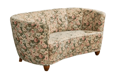A vintage-style, curved sofa upholstered in a floral fabric with a pastel color palette. The sofa features a rounded backrest with vertical channeling and integrated armrests that curve inwards. It is supported by four short, tapered wooden legs. — 3D model