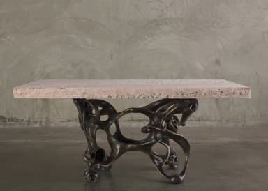 A console table with a rectangular, light pinkish-beige stone top and an intricately sculpted, dark bronze base. The base features an organic, abstract design with interconnected hollow forms and flowing lines, resembling bones or skeletal structures. The stone top has a rough-hewn edge and a textured surface with visible inclusions. — 3D model