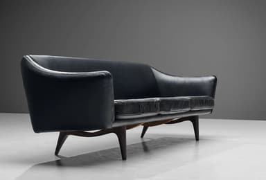 A three-seater sofa with a curved backrest and armrests, upholstered in dark leather. The seat is composed of three distinct cushions. The sofa is supported by four tapered wooden legs. — 3D model