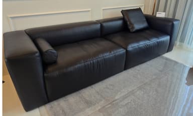 A contemporary black sectional sofa, comprising at least two modular segments, upholstered in what appears to be smooth black leather or a high-quality synthetic leather. It features clean lines, block-style armrests, and backrests, with a minimalist aesthetic. A single matching loose cushion is placed on one of the backrests. — 3D model