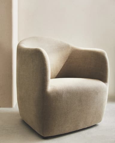 A contemporary upholstered armchair featuring a rounded, compact silhouette. The chair is entirely covered in a light beige, textured fabric, possibly boucle or a similar weave. It has a continuous backrest and integrated armrests that curve inward, creating a cocoon-like seating area. The base is subtly recessed, with small, dark glides barely visible beneath the main body. — 3D model
