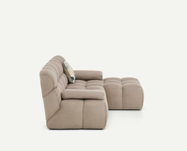 A light beige, modular sectional sofa featuring a chaise lounge component on the right side. The entire sofa is upholstered in a ribbed corduroy fabric, giving it a plush, textured appearance. It consists of deep, blocky cushions for both the seat and backrest, arranged in a low-profile, contemporary style. The armrests are similarly upholstered and integrated, providing a soft, rounded look. — 3D model