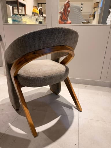 A contemporary armchair with a curved backrest and upholstered seat and arms. The frame appears to be constructed from wood, visible as a curved piece supporting the backrest. The upholstery is a textured fabric in a neutral tone. — 3D model
