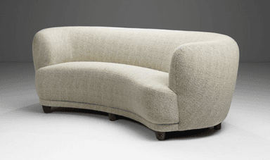 A curved, fully upholstered sofa featuring a serpentine form, rounded back and integrated armrests, and short, tapered wooden legs. It is covered in a light-colored, textured woven fabric. — 3D model