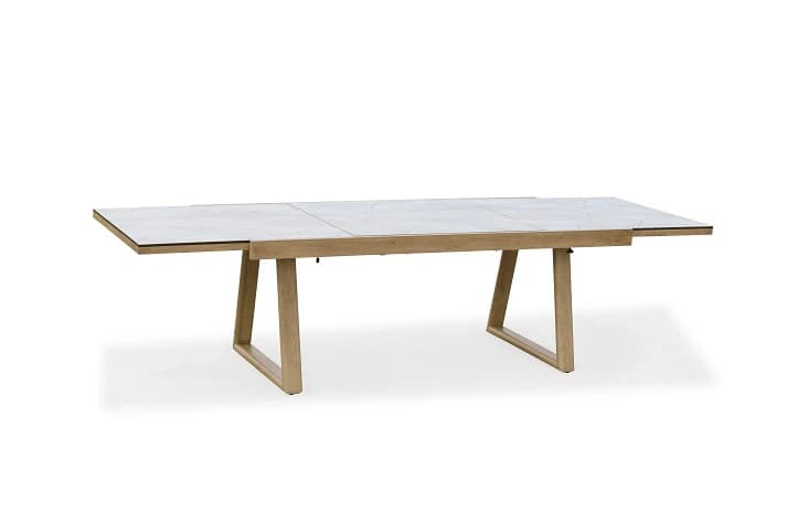 An extendable dining table with a light wood frame and a ceramic or stone-look top composed of multiple panels. The table features two angled legs on each side, connected by a lower horizontal support. The tabletop has a geometric pattern reminiscent of marble or terrazzo. — 3D model