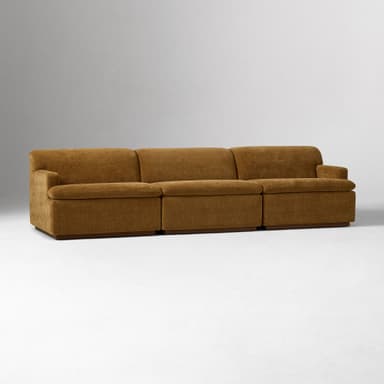 A close-up view of the armrest and side of a sofa. The sofa is upholstered in a textured, woven fabric with a brown hue. It features a rounded armrest that extends upwards and a rectangular base constructed from wood. — 3D model