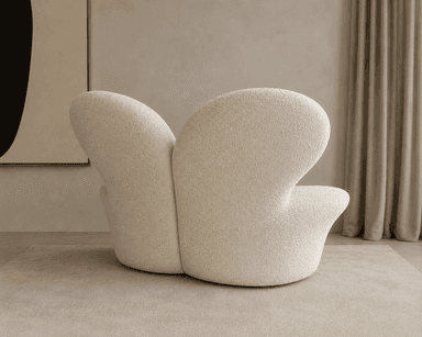 A sculptural, low-profile lounge chair upholstered in cream-colored bouclé fabric. The chair features a distinct organic form with smooth, continuous curves forming the seat, back, and integrated armrests. Its plush appearance suggests comfort, and the overall design is contemporary and minimalist, resting directly on the floor without visible legs. — 3D model