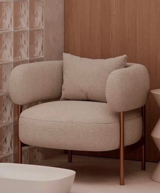 A single-seater upholstered chair featuring a curved back and integrated armrests, supported by an exposed, minimalist metal frame. It includes a separate back cushion and is covered in a soft, textured fabric in a light, neutral color. — 3D model