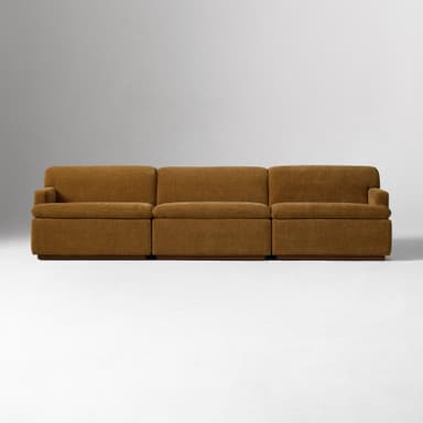 A close-up view of the armrest and side of a sofa. The sofa is upholstered in a textured, woven fabric with a brown hue. It features a rounded armrest that extends upwards and a rectangular base constructed from wood. — 3D model