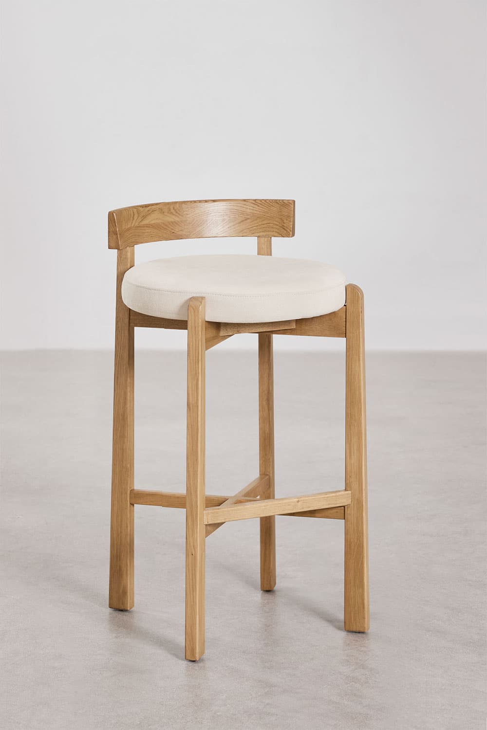 A modern bar stool featuring a light-toned oak wood frame and a circular cream upholstered seat. It has a low, gently curved backrest and a square-profile leg structure with an X-shaped cross-brace footrest. — 3D model