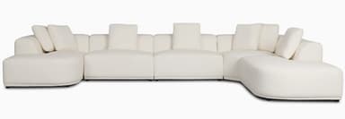 A large, contemporary modular U-shaped sectional sofa upholstered in a cream-colored fabric, featuring soft, rounded edges and a low-profile design, complete with multiple back cushions. — 3D model