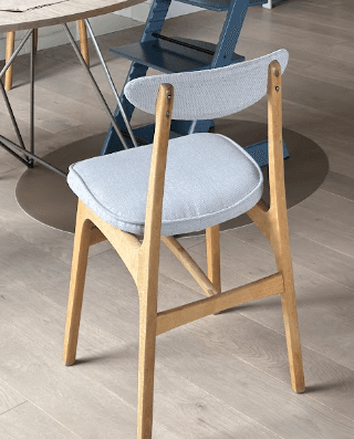 A modern dining chair with a light wooden frame and light grey fabric upholstery. The seat is a padded cushion, and the backrest is a curved, oval-shaped padded piece supported by the wooden frame. The chair features clean lines and a minimalist aesthetic. — 3D model