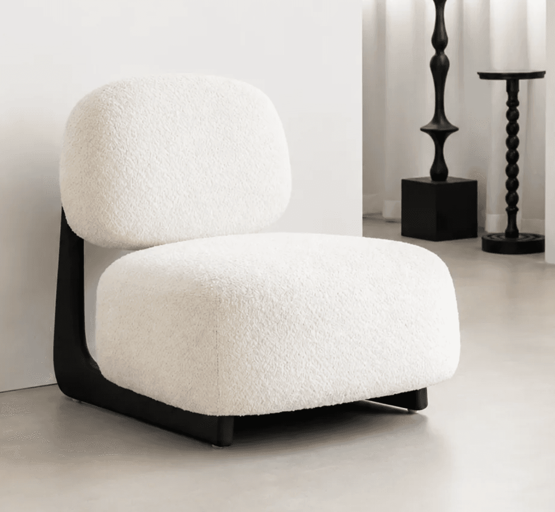 An armless, low-profile lounge chair featuring soft, rounded forms and upholstered in a textured off-white bouclé fabric. The seating and backrest cushions appear plush and inviting, supported by a distinctively shaped black base that provides a modern, minimalist foundation for the chair. — 3D model