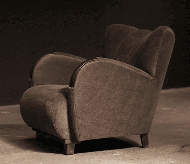 A robust, fully upholstered armchair viewed from the rear-right side, featuring a rounded backrest, integrated arms, and short, dark wooden legs. The chair is covered in a soft, dark taupe fabric. — 3D model