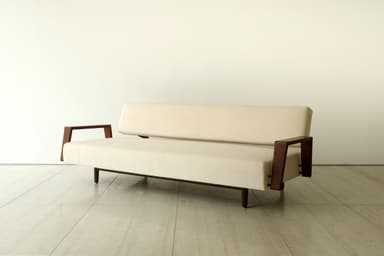 A minimalist two-seater loveseat featuring a cream-colored upholstered seat and backrest, supported by a dark, possibly walnut, wooden frame with open, U-shaped armrests and slender tapered legs. — 3D model