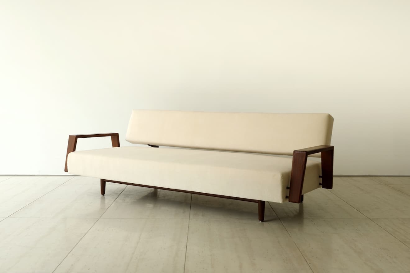 A minimalist two-seater loveseat featuring a cream-colored upholstered seat and backrest, supported by a dark, possibly walnut, wooden frame with open, U-shaped armrests and slender tapered legs. — 3D model