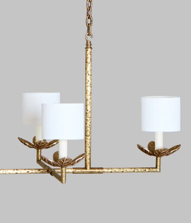 A linear chandelier suspended by two chains. The fixture has a horizontal bar with six lights, each featuring a white cylindrical lampshade supported by a decorative metal arm with leaf-like accents. The metal frame has a distressed gold finish. — 3D model