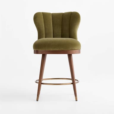 A stylish bar stool featuring an olive green velvet upholstered seat and a distinctive scalloped, channel-tufted backrest. It stands on four angled wooden legs, connected by a circular brass footrest, and finished with brass ferrules on the feet. The design blends luxurious materials with mid-century modern influences. — 3D model
