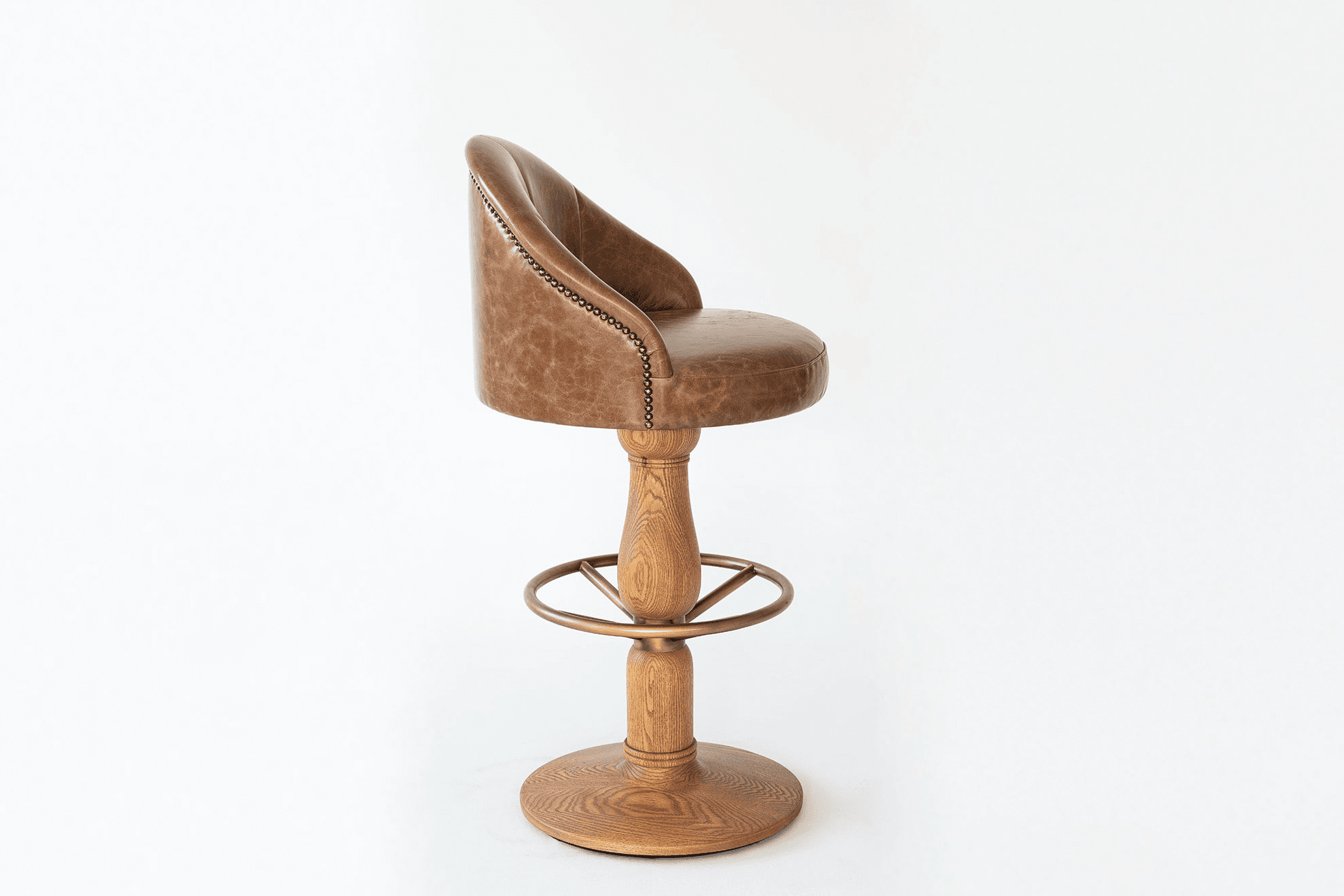 A brown, distressed leather bar stool featuring a curved, partially enclosed back with decorative nailhead trim, a round padded seat, and a turned wooden pedestal base with a circular brass footrest. The base terminates in a wide, stable round wooden disc. — 3D model