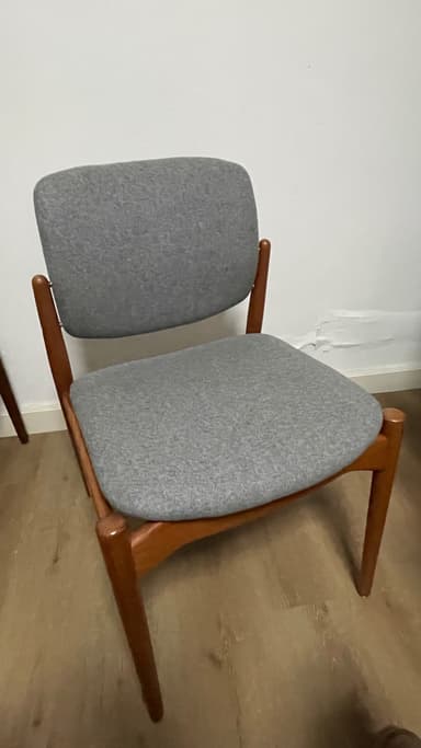 An armless dining chair featuring a minimalist design with a visible wooden frame and upholstered seat and backrest. The frame appears to be made of a warm-toned wood, possibly teak, with tapered legs. Both the seat and the slightly curved backrest are upholstered in a light grey fabric, providing a clean and contemporary aesthetic often associated with Scandinavian or Mid-Century Modern design. — 3D model