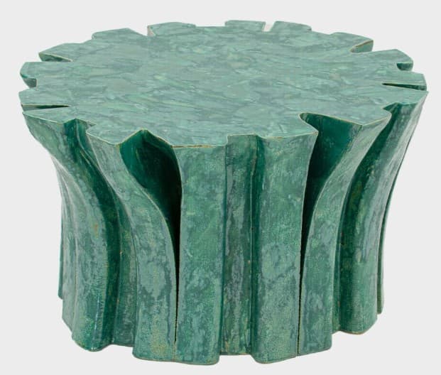 A sculptural pedestal table featuring an organic, biomorphic design and a rich green finish. The table has a circular top with an irregularly scalloped edge, resembling a stylized leaf or natural formation. The base is composed of undulating, vertical elements that create a fluted or pleated effect, giving the piece a fluid and naturalistic appearance. The surface has a mottled, textured patina, suggesting either a ceramic, concrete, or composite material with a malachite-inspired glaze or finish. — 3D model