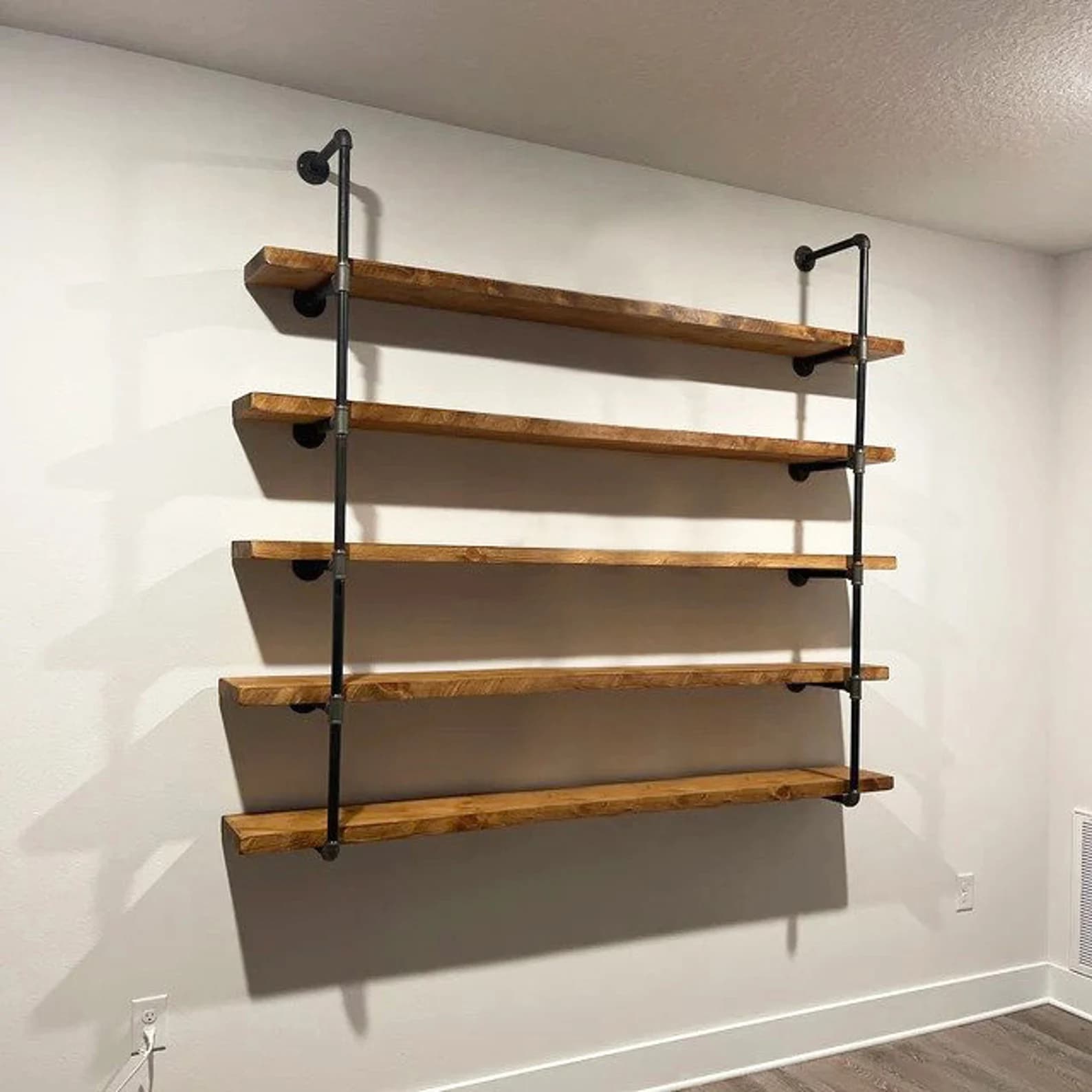 A multi-tiered wall-mounted shelf unit constructed from wooden planks and industrial-style black metal pipes. The shelves appear to be made of solid wood with a natural finish, showcasing some grain texture. The support structure consists of vertical pipes with horizontal pipe sections extending to hold the shelves. The assembly suggests an industrial or rustic aesthetic. — 3D model