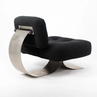 A postmodern lounge chair featuring a distinctive sculptural brushed metal base supporting a plush, black upholstered seat and backrest. The base is formed by a continuous, wide C-shaped metal band that curves elegantly from the floor, up to support the back, and then back down to form the front leg structure. The seat and back are generously padded and upholstered in black fabric, with subtle button tufting on the seat. The backrest is affixed to the metal support with visible hardware, including two black spherical elements. — 3D model