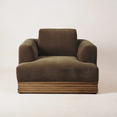 A single-seater armchair with a plush, upholstered body and a distinct wooden base. The armchair features a deep seat, substantial armrests, and a high back cushion. The base is constructed from horizontally oriented wooden slats with a textured finish, providing a contrast to the soft upholstery. — 3D model