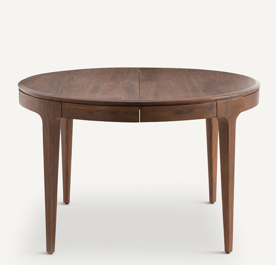 A round dining table with a wooden top and four tapered legs. The tabletop appears to be composed of two sections that meet in the middle, suggesting it might be extendable. The legs have a subtle outward curve and are angled for support. The wood grain is visible and has a rich, dark brown color. — 3D model