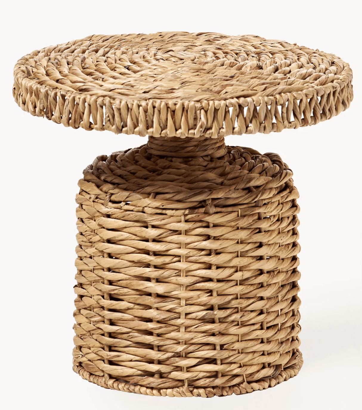 A small, round pedestal accent table crafted entirely from woven natural fibers, likely seagrass or water hyacinth. It features a solid cylindrical base that tapers slightly towards a smaller central column, which supports a thick, round tabletop. The weaving exhibits varying patterns, with a tighter, spiraled weave on the tabletop and a more open, basket-like weave on the cylindrical base. The table has a natural, earthy tone. — 3D model