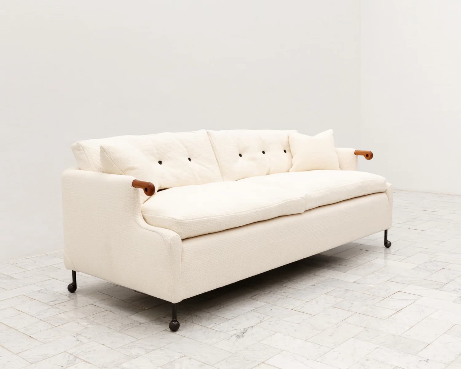 A three-seater sofa featuring a cream-colored, textured fabric upholstery. The design incorporates distinctive exposed wooden armrests that curve elegantly, complementing the otherwise upholstered frame. The sofa has loose seat cushions and back cushions, the latter featuring three dark button tufts. It is supported by slender, recessed black metal legs with small castor-like feet. — 3D model