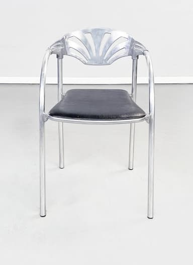 A contemporary armchair featuring a polished aluminum frame with gracefully curved armrests and legs. The backrest showcases a distinctive fan-shaped design with decorative cutouts, while the seat is a comfortable black padded cushion. — 3D model