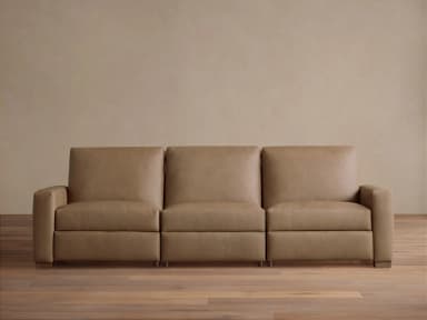 A modern three-seater sofa upholstered in a light tan or beige leather-like material. It features three individual seat and back cushions, block arms, and short, rectangular wooden feet. The design is sleek and contemporary, with the rightmost seat appearing to have reclining functionality indicated by a control panel on the inner arm. — 3D model