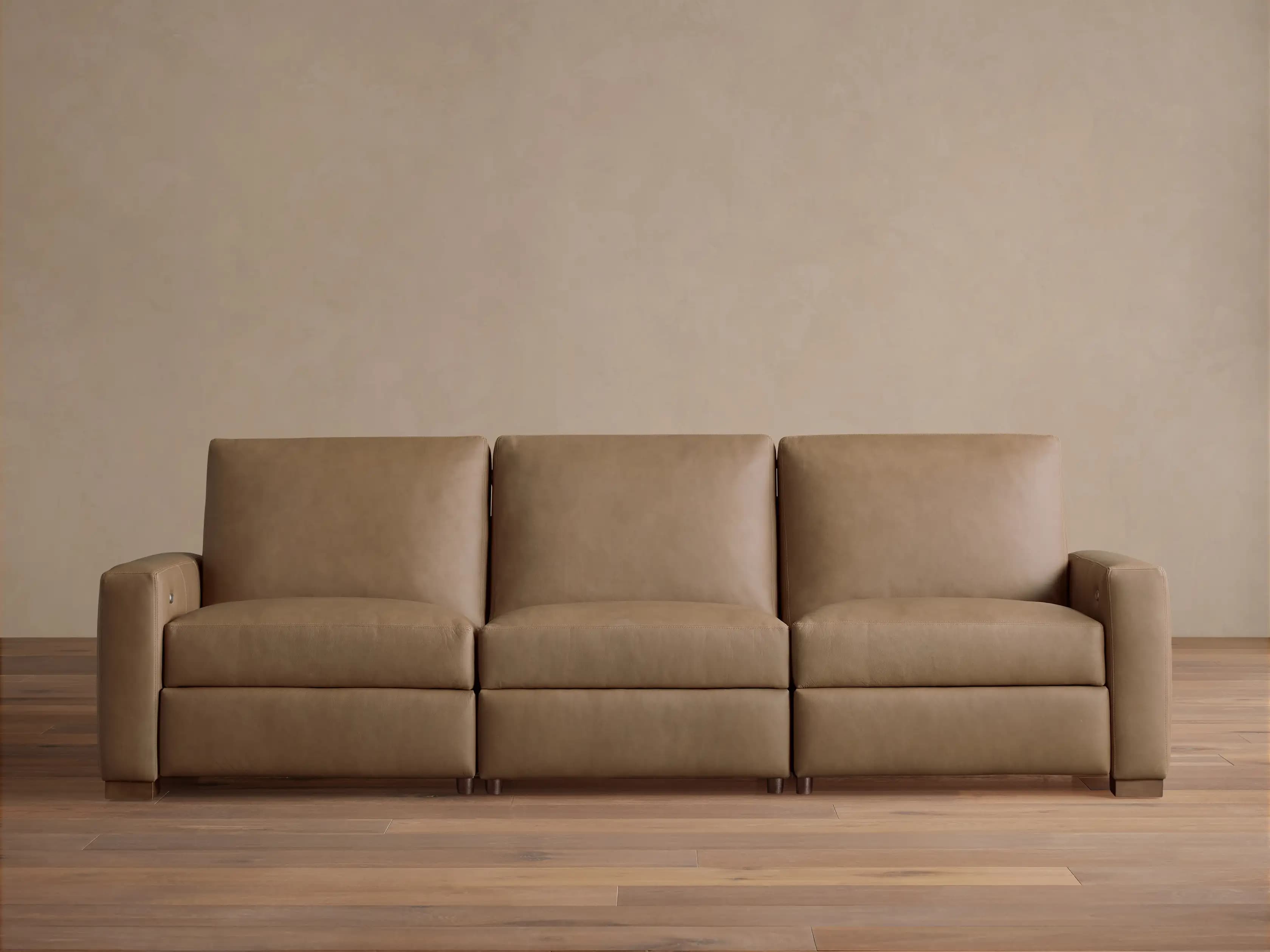 A modern three-seater sofa upholstered in a light tan or beige leather-like material. It features three individual seat and back cushions, block arms, and short, rectangular wooden feet. The design is sleek and contemporary, with the rightmost seat appearing to have reclining functionality indicated by a control panel on the inner arm. — 3D model