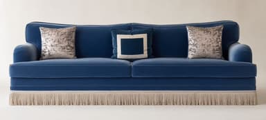 A luxurious three-seater sofa upholstered in deep blue velvet, featuring a distinctive gently curved back, rolled armrests, and an elaborate fringe skirting its base. It is accessorized with three decorative accent pillows. — 3D model