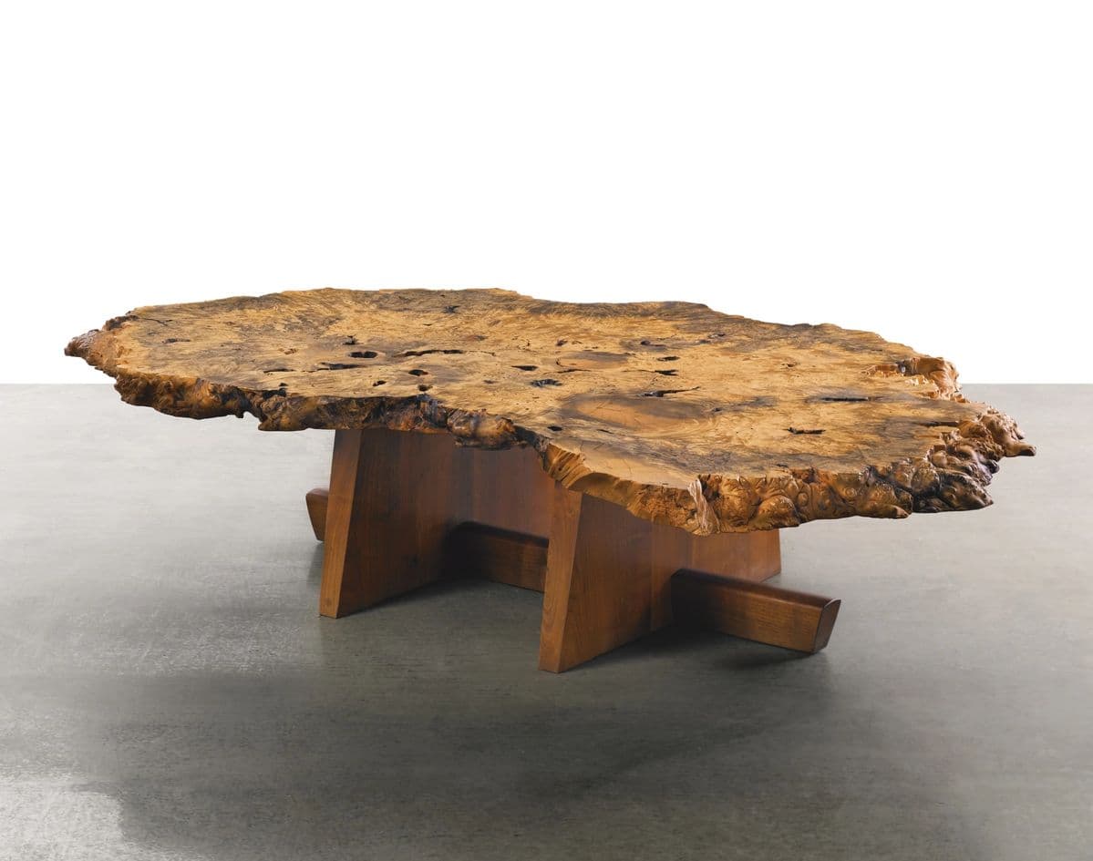 A unique coffee table featuring a large, freeform slab of burl wood as the tabletop, supported by a geometric wooden base. The tabletop exhibits natural, irregular edges with visible wood grain, knots, and voids, showcasing the organic form of the burl. The base consists of two trapezoidal wooden supports connected by a horizontal wooden beam. — 3D model