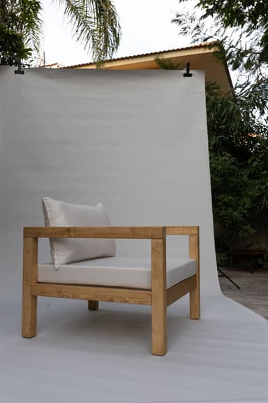A single armchair with a solid wood frame and upholstered cushions. The frame consists of thick, square-profile wooden beams for the legs, base, and arms. The seat and back are padded with white cushions. A rectangular lumbar pillow is placed against the back cushion. — 3D model