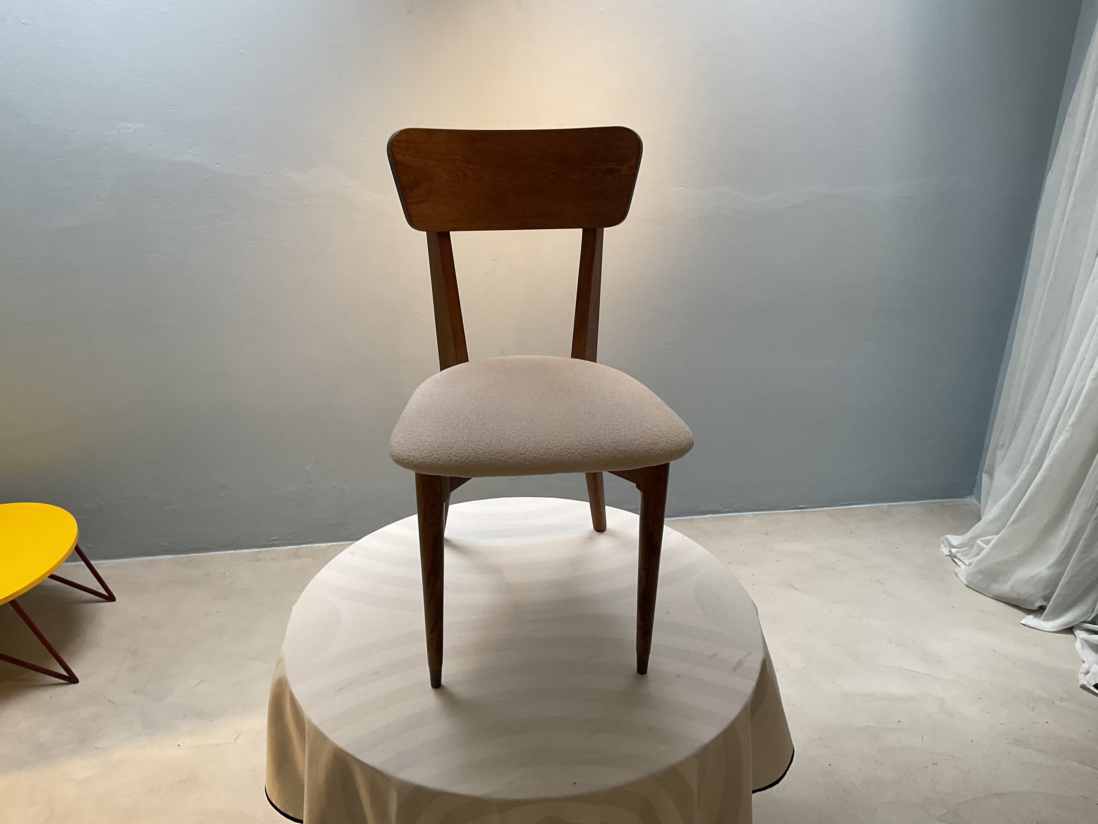 A wooden chair with a cushioned seat, positioned on a round table covered with a tablecloth. The chair has a curved backrest and four legs. The seat is upholstered in a textured fabric. — 3D model