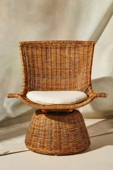 A contemporary lounge chair crafted from natural woven rattan, featuring a wide, curving backrest and a conical base that allows for 360-degree swivel movement. It includes a round, off-white seat cushion for added comfort. — 3D model