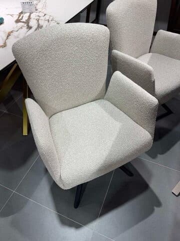 An upholstered armchair featuring a rounded backrest, integrated armrests, and splayed, tapered legs. The chair is covered in a light, textured fabric, likely a cream or off-white color, and the legs are finished in black. Its design suggests a modern or contemporary aesthetic, suitable for various interior settings. — 3D model