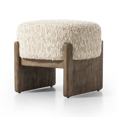 A rectangular ottoman with a textured, boucle-like upholstery in a neutral cream color. It is supported by a sturdy wooden base with two block-style legs at the front and two at the back, connected by a horizontal wooden beam. — 3D model