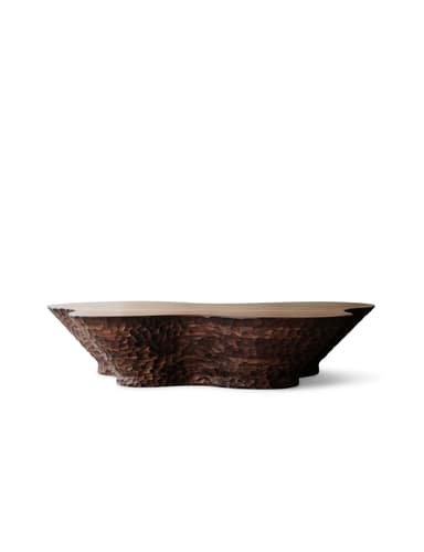 A low, wide coffee table made of dark wood, featuring a smooth top surface and highly textured, hand-carved sides and base. The shape is organic and irregular, resembling a natural formation with a rugged, chiseled aesthetic. — 3D model