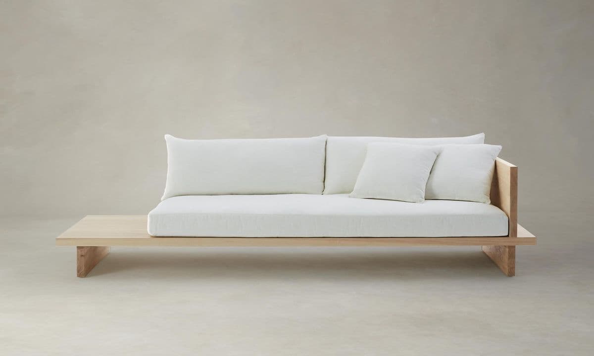 A low-profile sofa featuring a wooden base and frame with a wide, integrated side table. The seating area is covered with white cushions and throw pillows. — 3D model