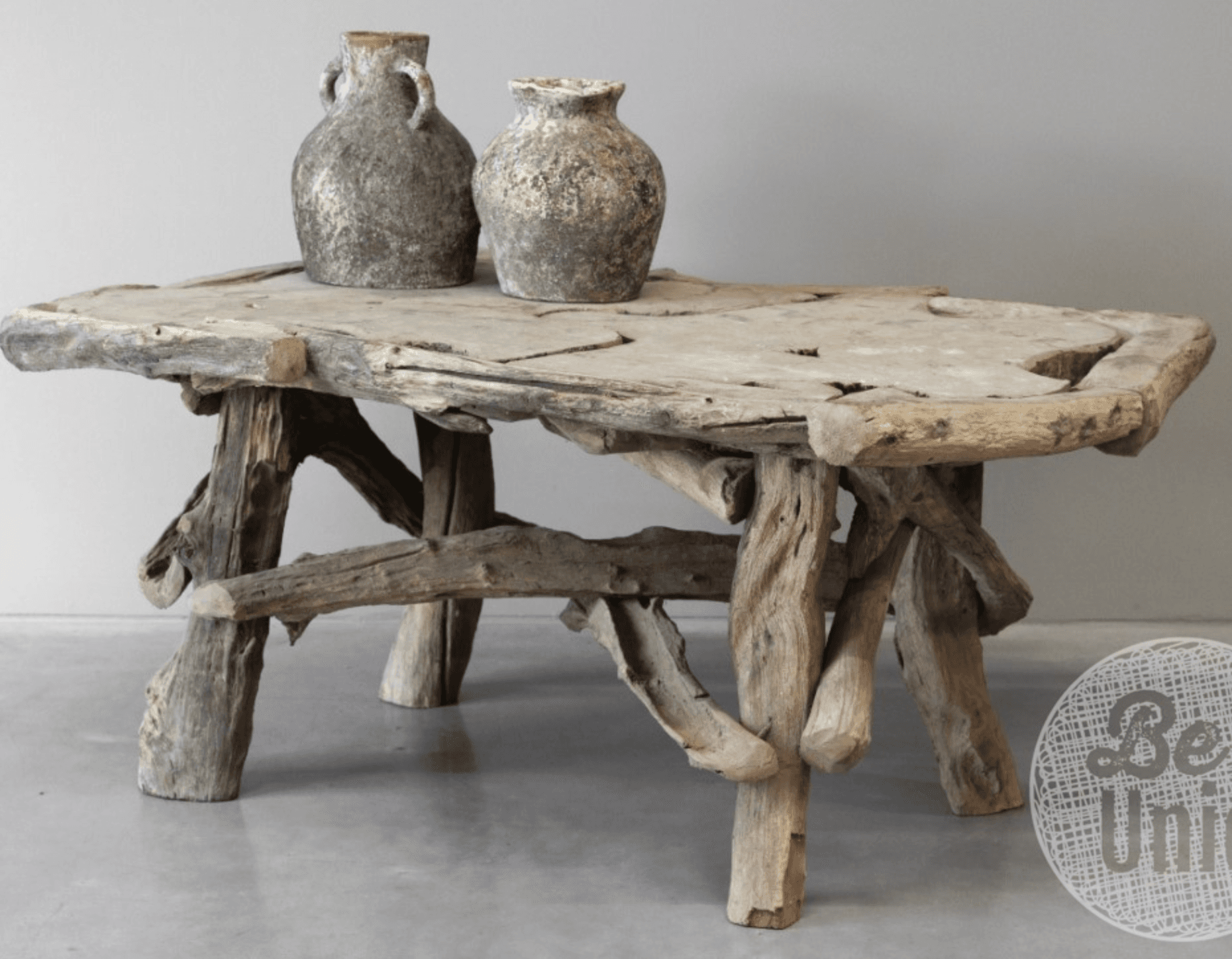 A rustic coffee table crafted entirely from natural, weathered wood, likely driftwood or reclaimed timber. It features an irregularly shaped, live edge tabletop with visible fissures and a natural, aged patina. The base is composed of multiple branch-like supports, uniquely assembled to form a stable and organic foundation, reflecting a handcrafted aesthetic. — 3D model
