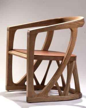 A contemporary armchair crafted from light-colored solid wood, featuring a gracefully curved backrest and integrated armrests. The chair incorporates a geometric, sculptural base with multiple intersecting wooden struts providing support. A contrasting reddish-brown leather cushion forms the seat, complementing the natural wood tone. — 3D model