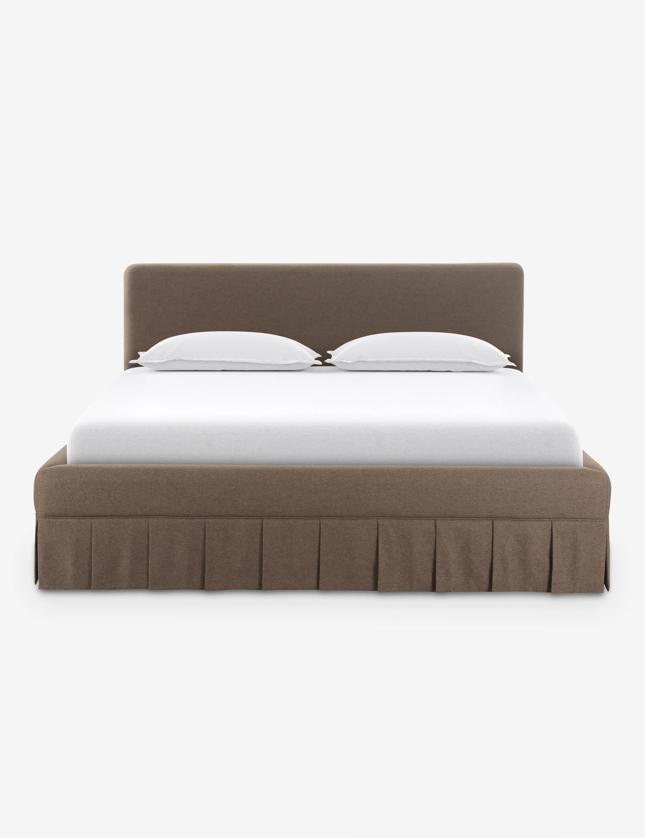 A contemporary upholstered platform bed featuring a soft, rounded headboard and a matching base with an integrated pleated bed skirt. The bed is rendered with a white mattress and two white pillows, suggesting a complete sleep system. The upholstery has a textured, fabric appearance in a neutral brown or taupe color. — 3D model
