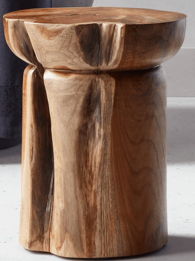 A sculptural solid teak wood stool with an organic design. It features a rounded top with subtly scalloped edges and three thick, curved legs that are seamlessly integrated into the top, creating a sturdy and cohesive form. The natural wood grain is prominent throughout the piece. — 3D model