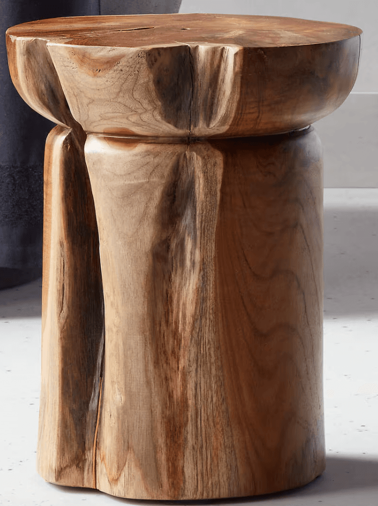 A sculptural solid teak wood stool with an organic design. It features a rounded top with subtly scalloped edges and three thick, curved legs that are seamlessly integrated into the top, creating a sturdy and cohesive form. The natural wood grain is prominent throughout the piece. — 3D model